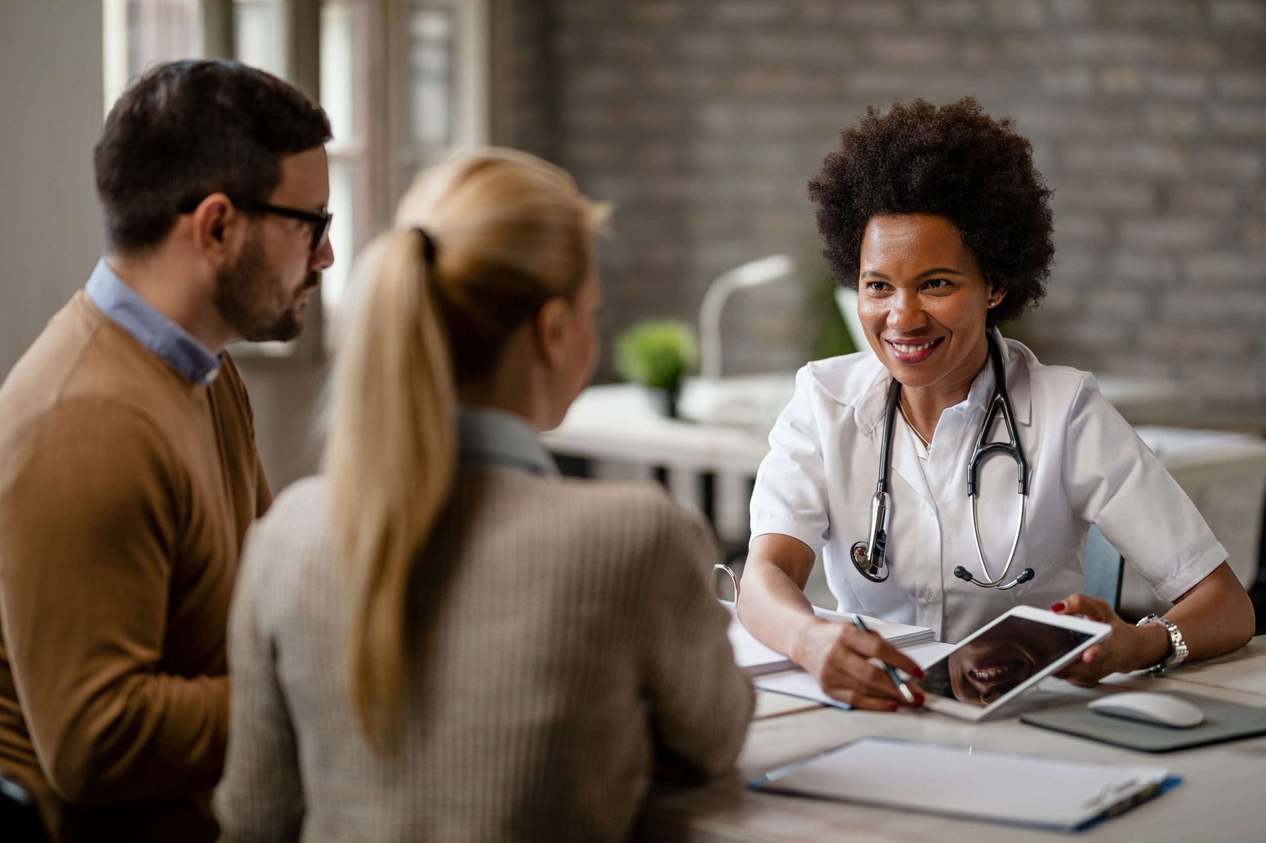 happy-black-female-doctor-talking-couple-showing-them-medical-test-results-touchpad-during-consultations-clinic-scaled.jpg