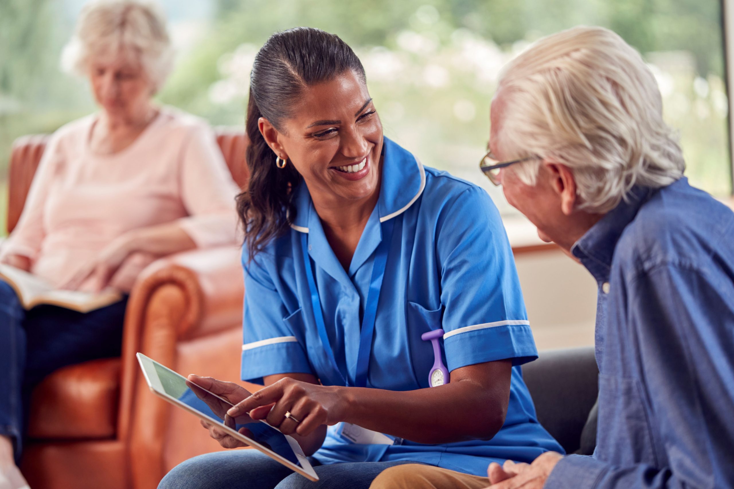 senior-couple-home-with-man-talking-female-nurse-care-worker-using-digital-tablet-2-scaled.jpg