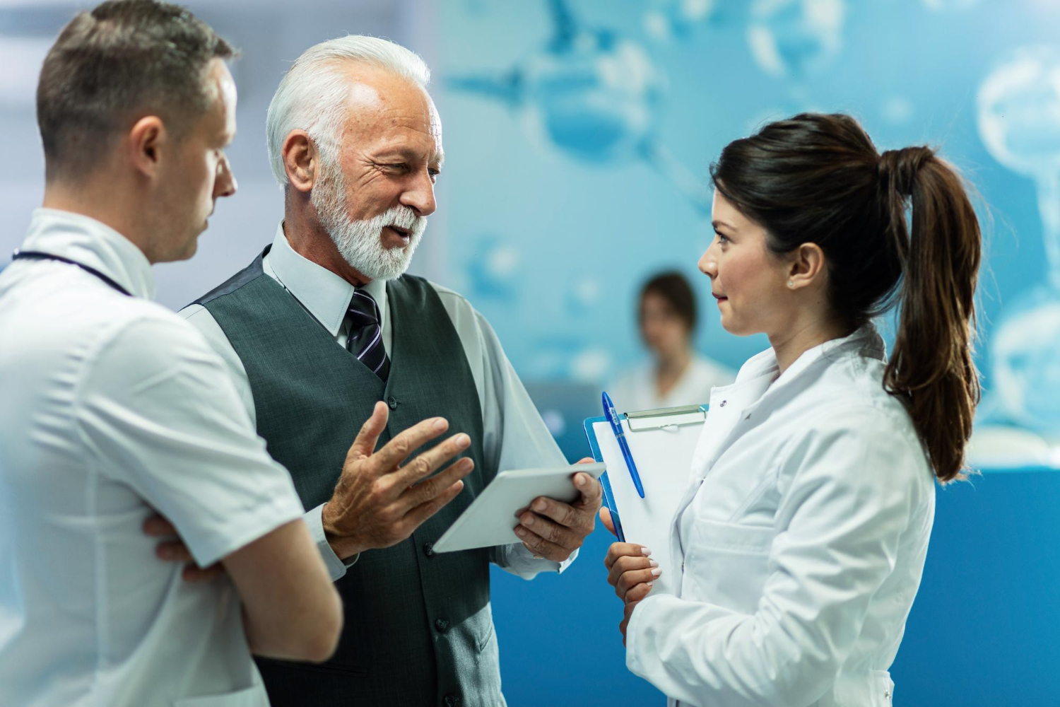 happy-mature-businessman-using-digital-tablet-while-talking-healthcare-workers-hallway-clinic.jpg